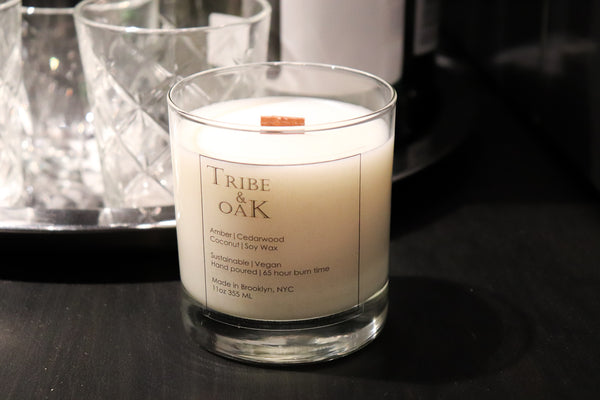A close-up of our coconut-soy, wooden wick, 11-oz Amber Cedarwood scented candle from Tribe & Oak is sitting on a dining room table.